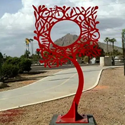 art piece of a red metal tree with a open spot in the middle that frames the mountains when looking through it.